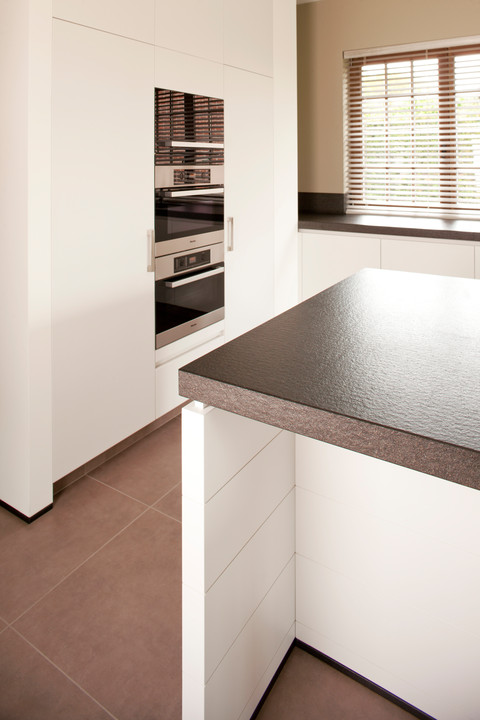 WoonProject Aalter maakte deze mooie moderne keuken op maat. Op de foto ziet u het granieten geborsteld werkblad en de wit gelakte fronten.