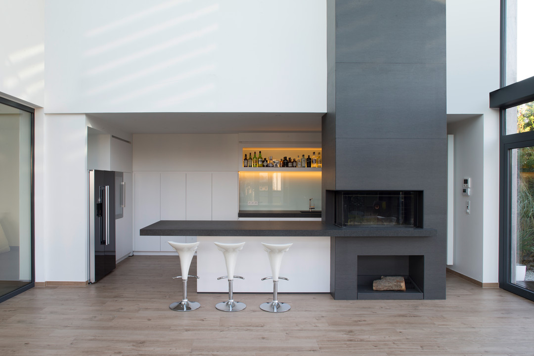 Deze moderne keuken met wit gelakte kasten en een werkblad in natuursteen werd ontworpen en geplaatst door WoonProject Aalter. De haard geeft een warme toets aan het strakke interieur.